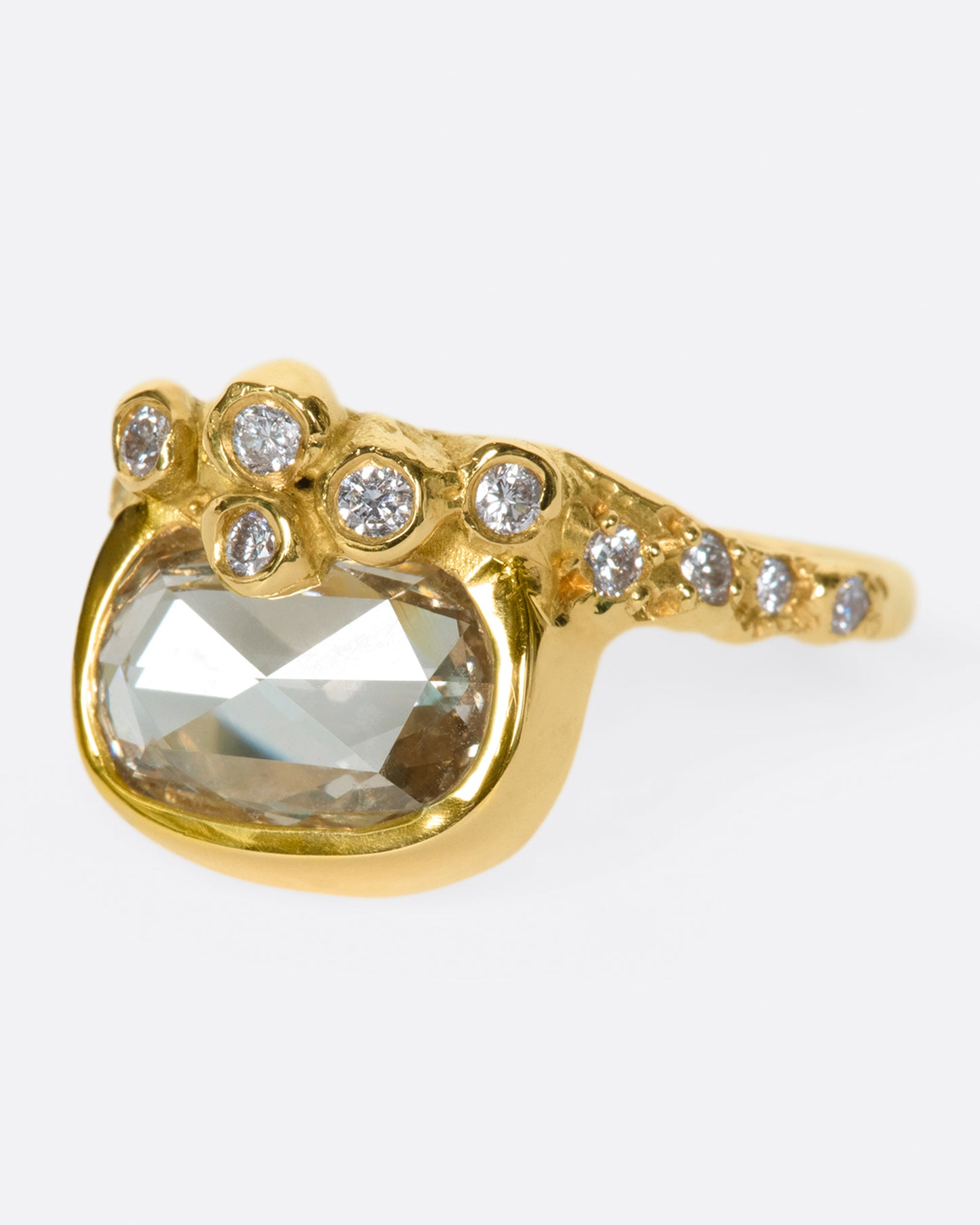 A yellow gold ring with an oval rose cut diamond sits atop an anemone-inspired band dotted with diamonds.