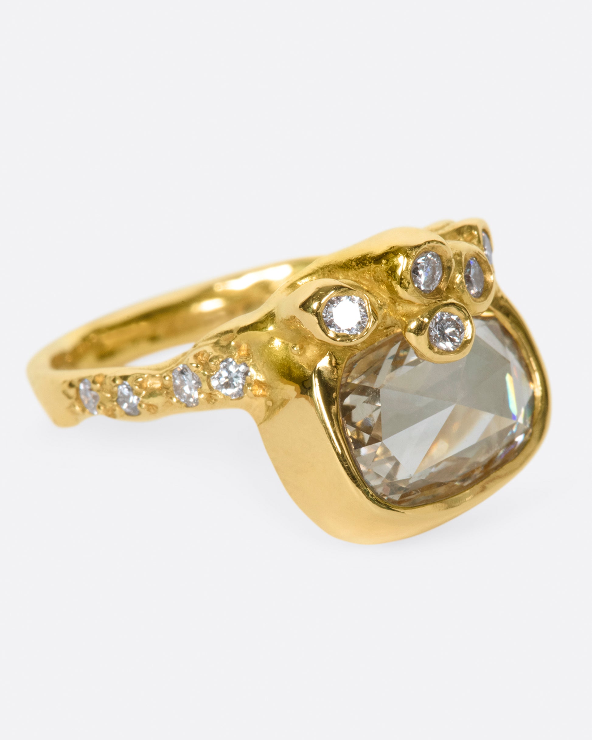 A yellow gold ring with an oval rose cut diamond sits atop an anemone-inspired band dotted with diamonds.