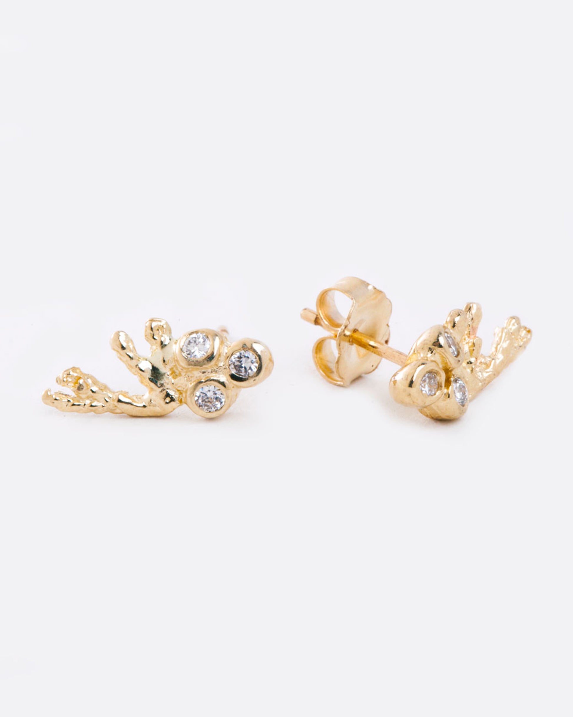 two yellow gold earrings with a trio of diamonds bezel set, and a yellow gold branch extending to the side. the earring on the right is on a 45 degree angle and shows the butterfly backing.