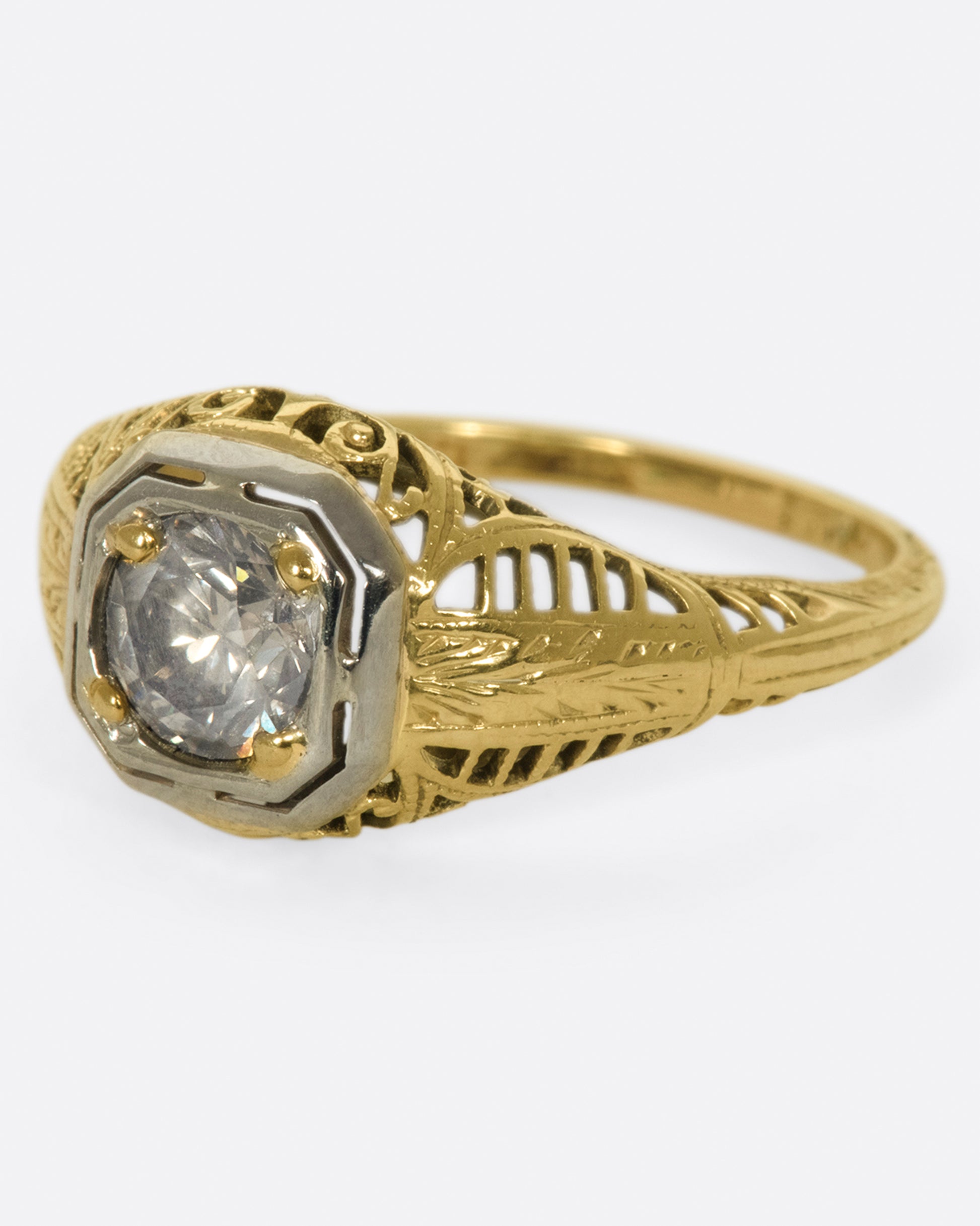 A filigree-covered signet ring with a champagne diamond at its center, set in a white gold bezel.