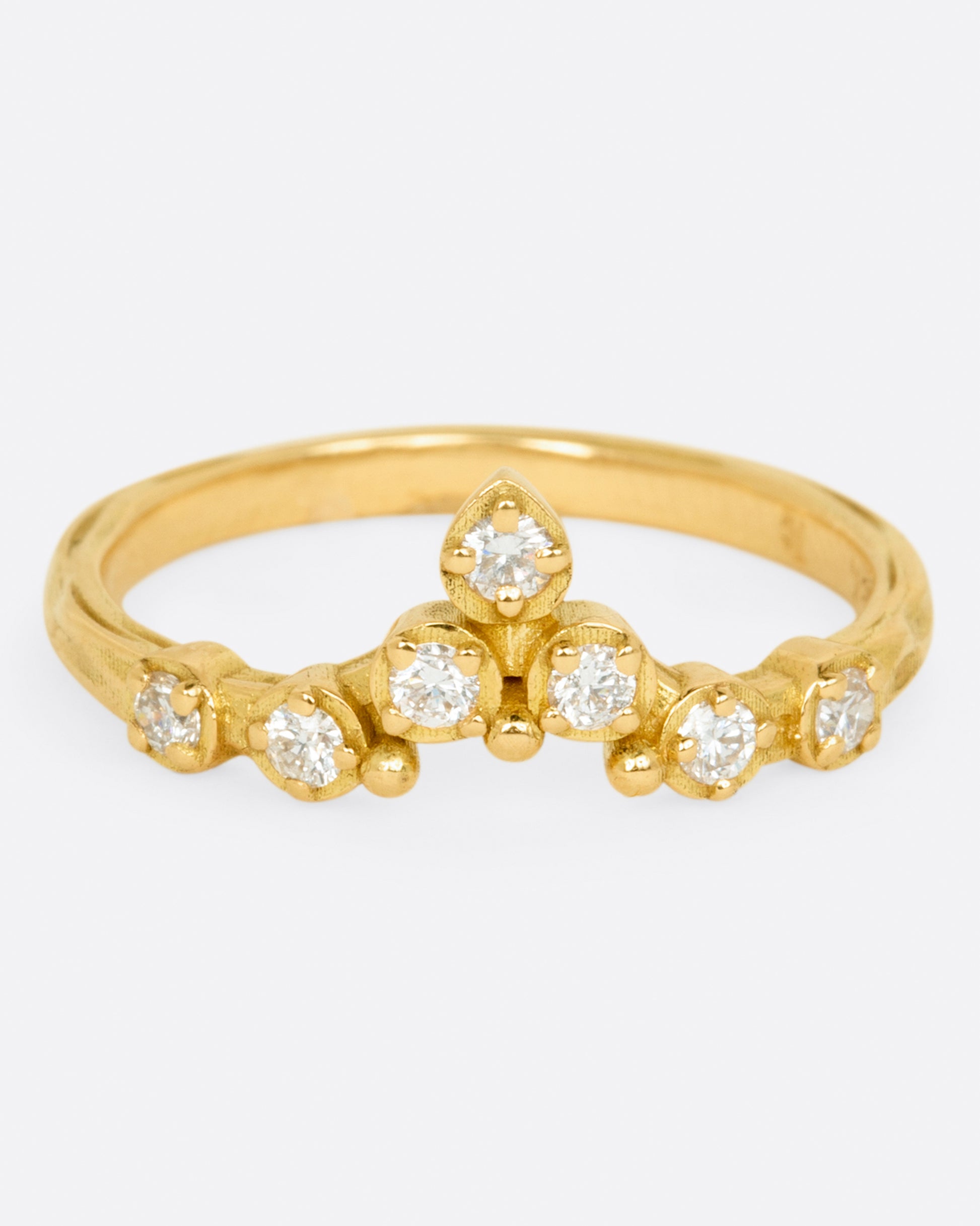 A slightly curved and pointed ring with seven diamonds on a textured band.