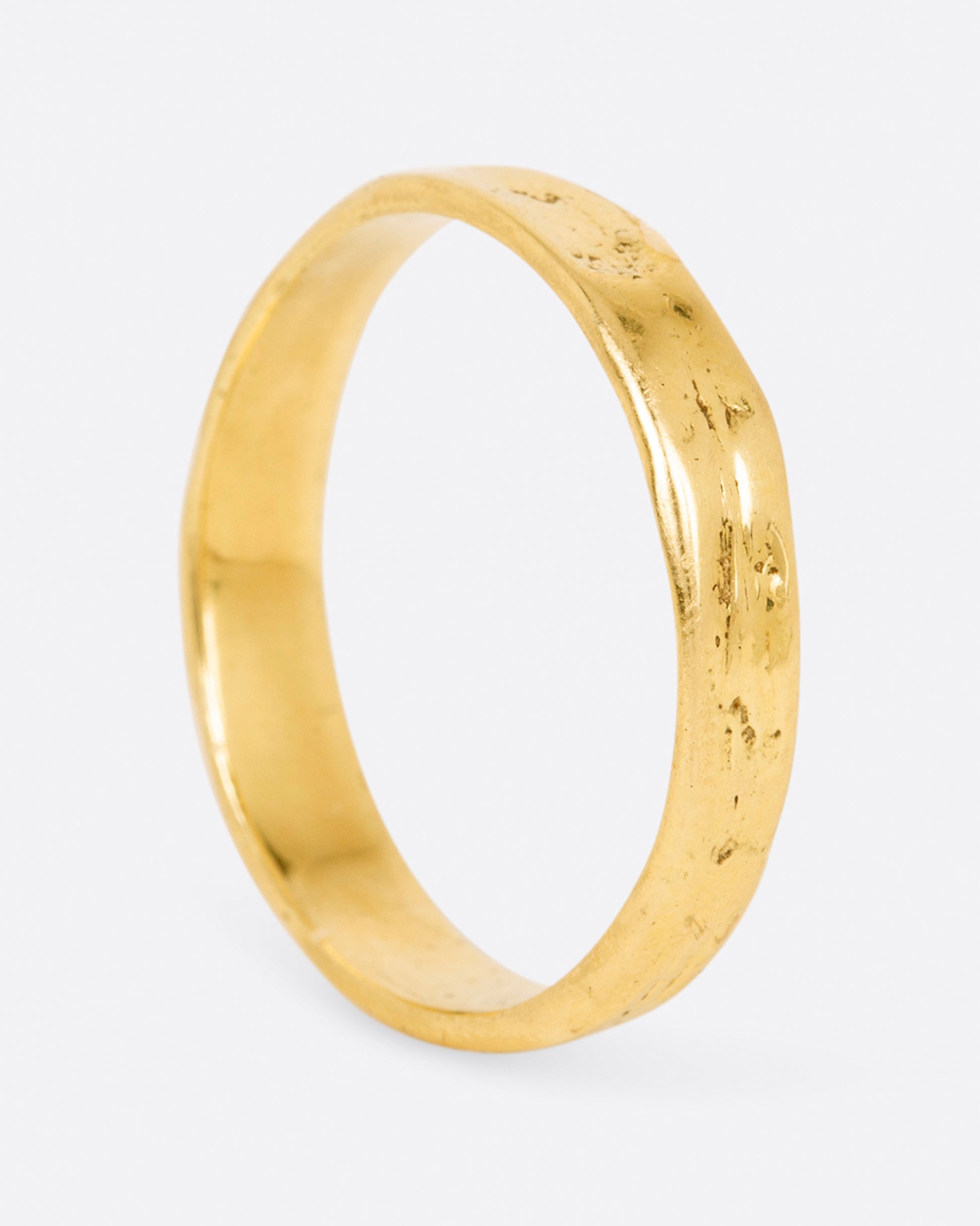 A textured yellow gold band that is meant to look worn in, shown standing up.