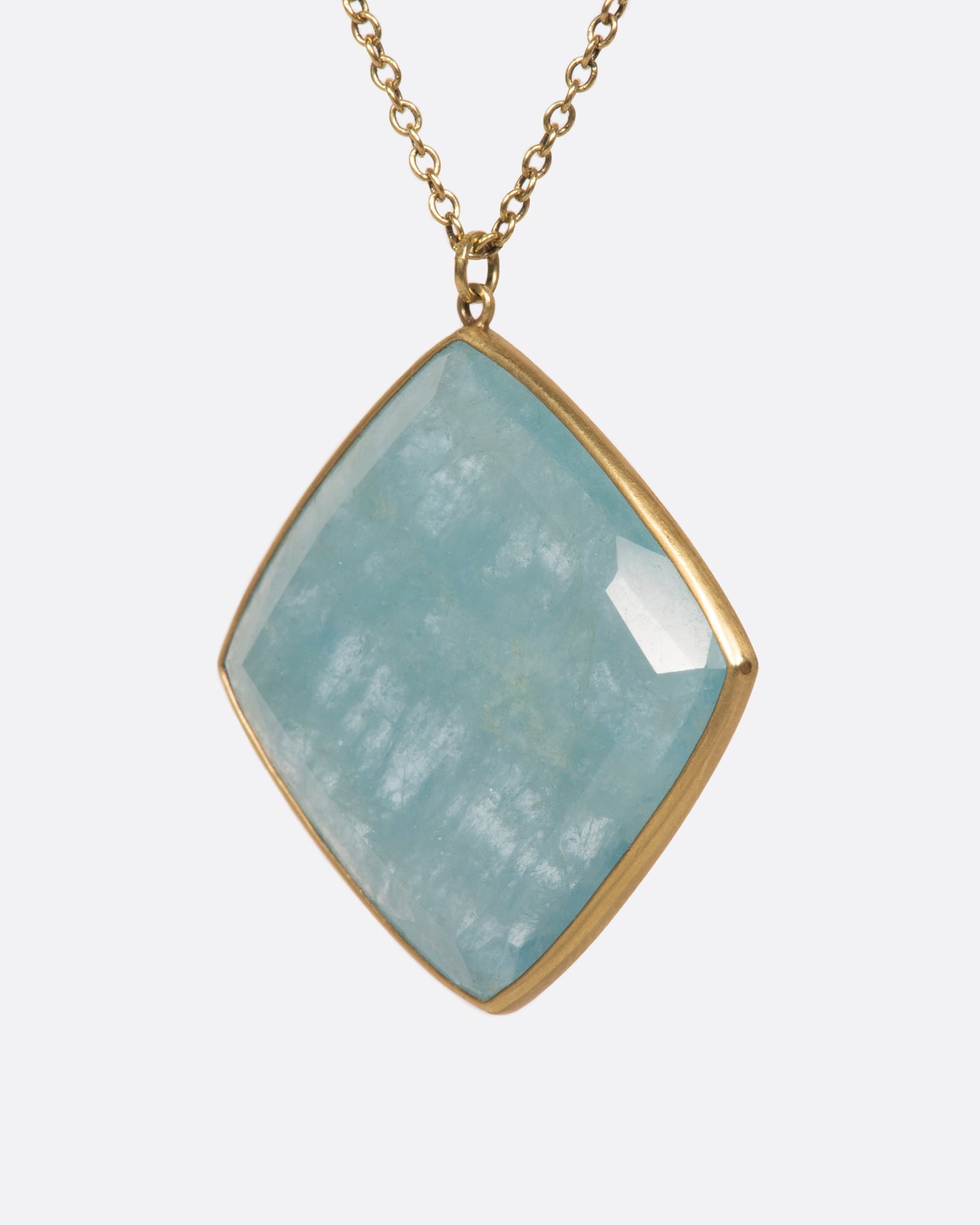 A large square aquamarine pendant hangings on a green gold chain, shown from the side.