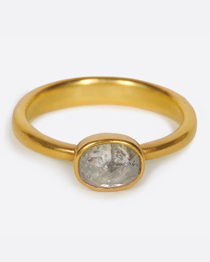 A pale grey, rose cut, oval diamond. Set horizontally on a simple, yellow gold band. Shown from the front.