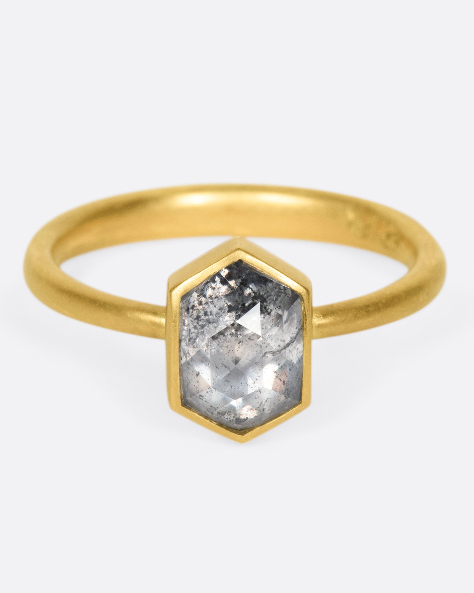 A salt and peppery hexagonal diamond shines in a bezel setting atop this ring.