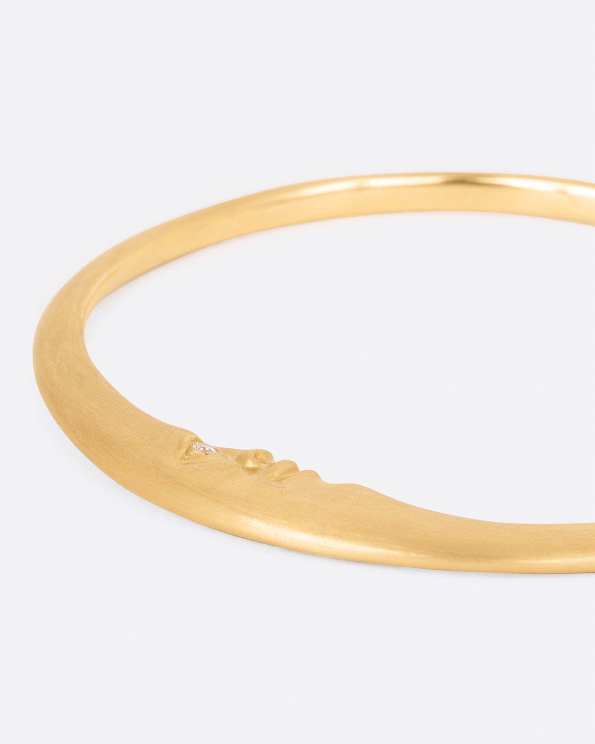 A yellow gold bangle bracelet with a moonface and diamond eyes, shown from the back.