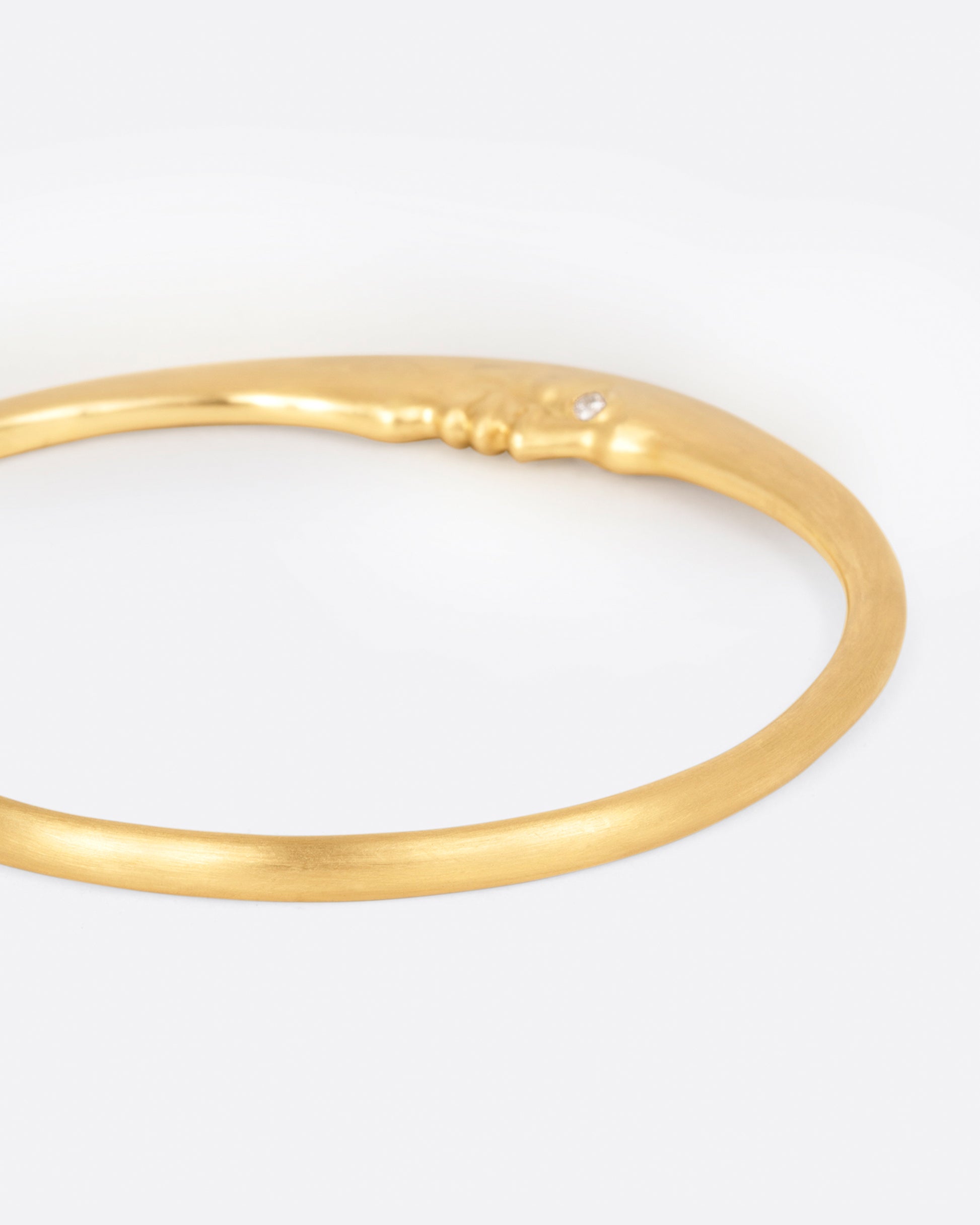 A yellow gold bangle bracelet with a moonface and diamond eyes, shown from the side.