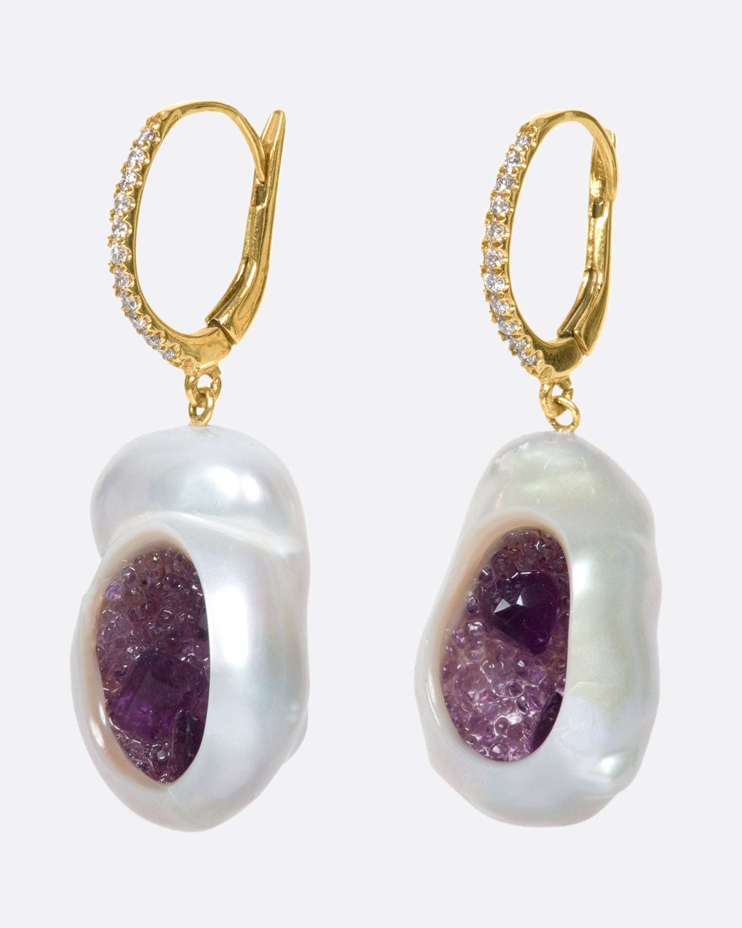 two dangle drop earrings hanging and viewed from the side. the drop is a pearl that has been partially carved out and lined with amethysts. the yellow gold hooks have pave diamonds on the bail.