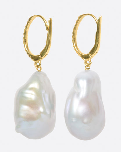 A pair of dangle earrings with carved out pearls lined with amethysts. Each earring is topped with  yellow gold ear hook with pave diamonds. Shown from the back.