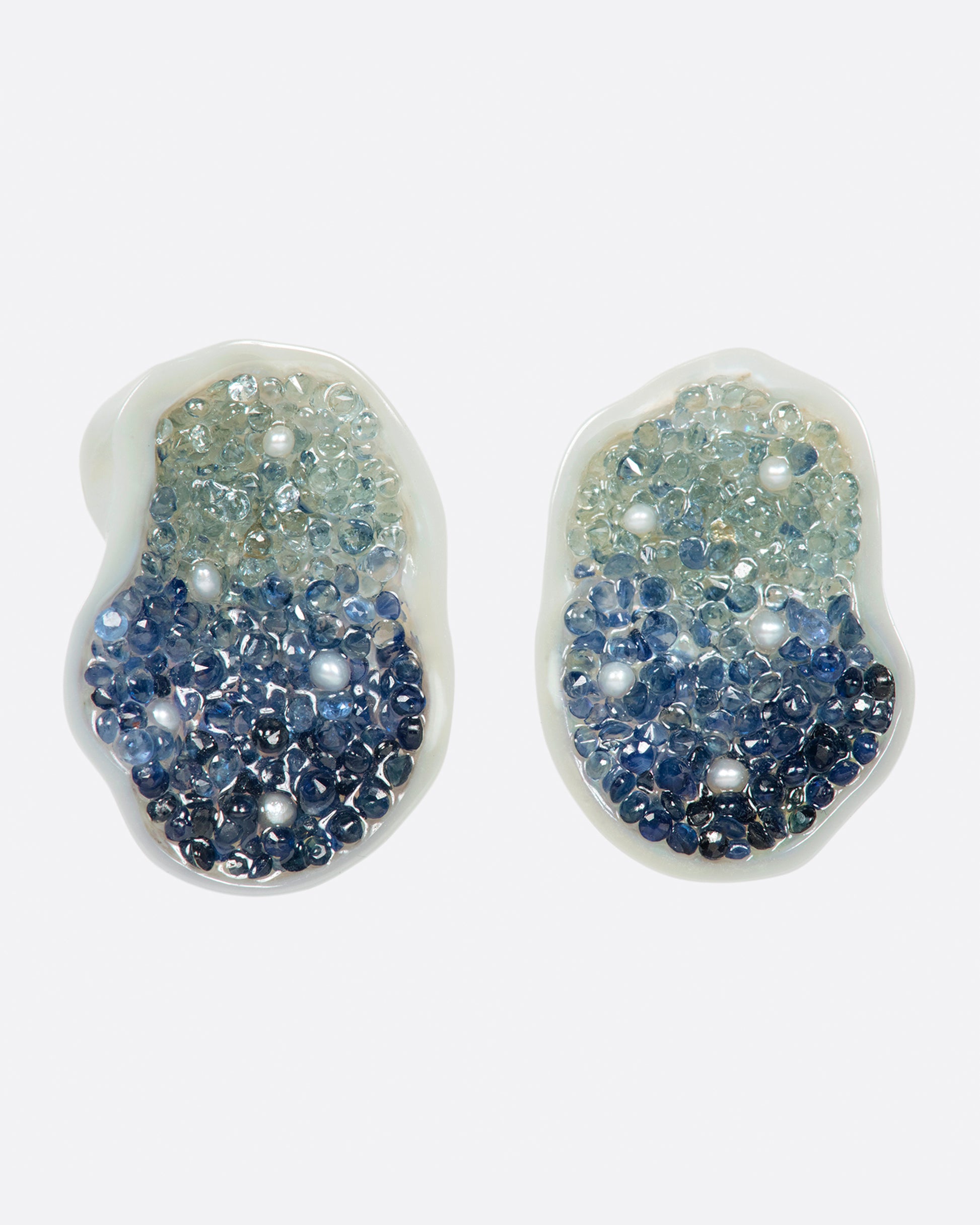 A pair of stud earrings made from halves on one freshwater soufflé pearl, lined with blue sapphires and seed pearls.
