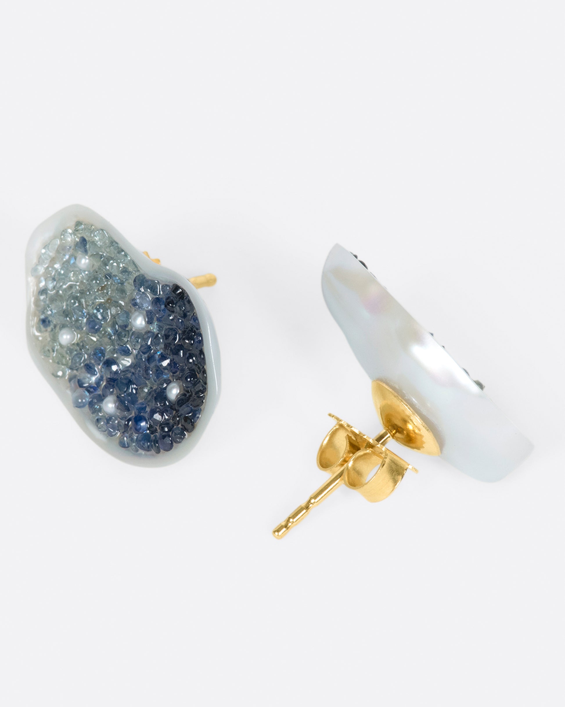 A pair of stud earrings made from halves on one freshwater soufflé pearl, lined with blue sapphires and seed pearls.