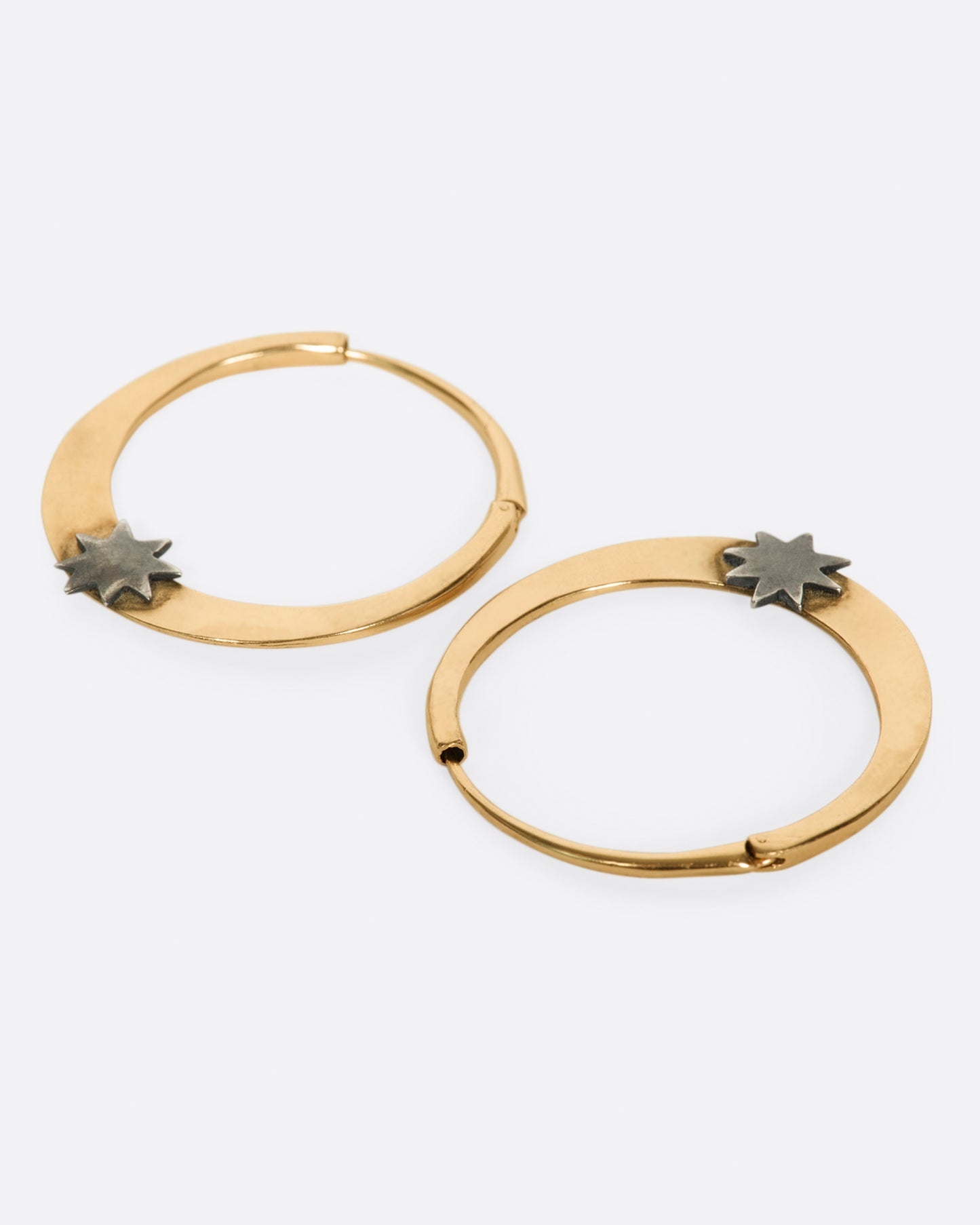 A pair of rose gold tapered hoop earrings with sterling silver stars at their base, shown laying flat.