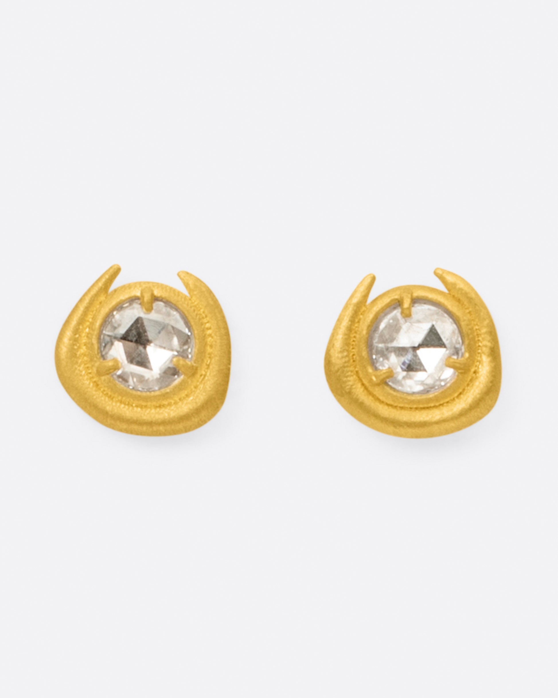 A pair of semi-circular high karat gold stud earrings with a rose cut diamond at their centers, shown from the front.