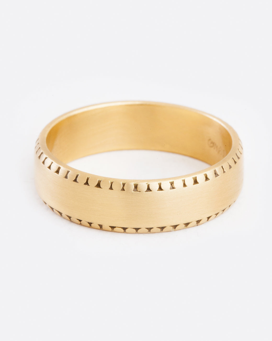 A front view of a yellow gold ring with a matte finish. The edges of the ring has light small dots around the top and bottom. They aren't super strong and almost look slightly worn away.