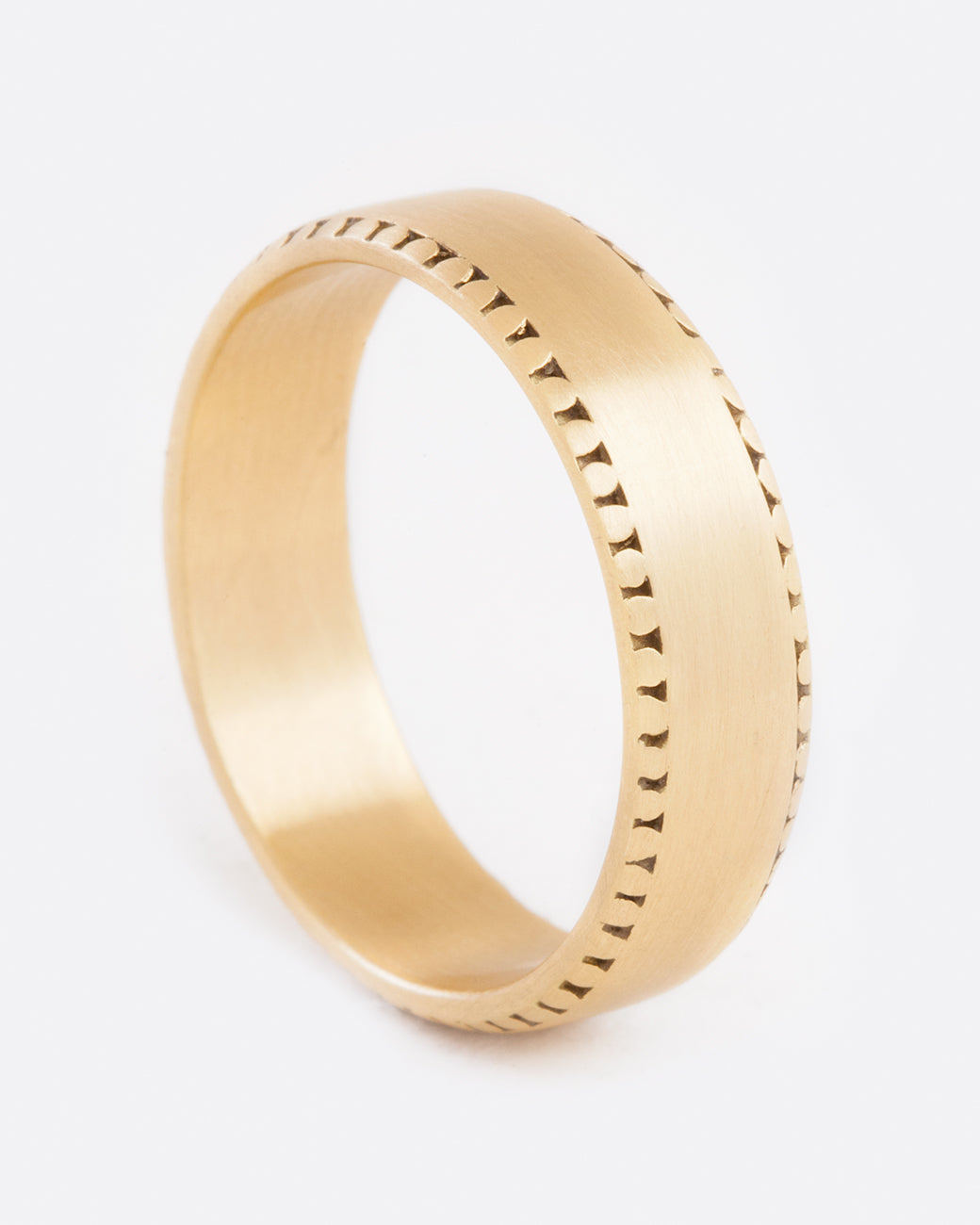 A front view of a yellow gold ring with a matte finish. The edges of the ring has light small dots around the top and bottom. They aren't super strong and almost look slightly worn away.