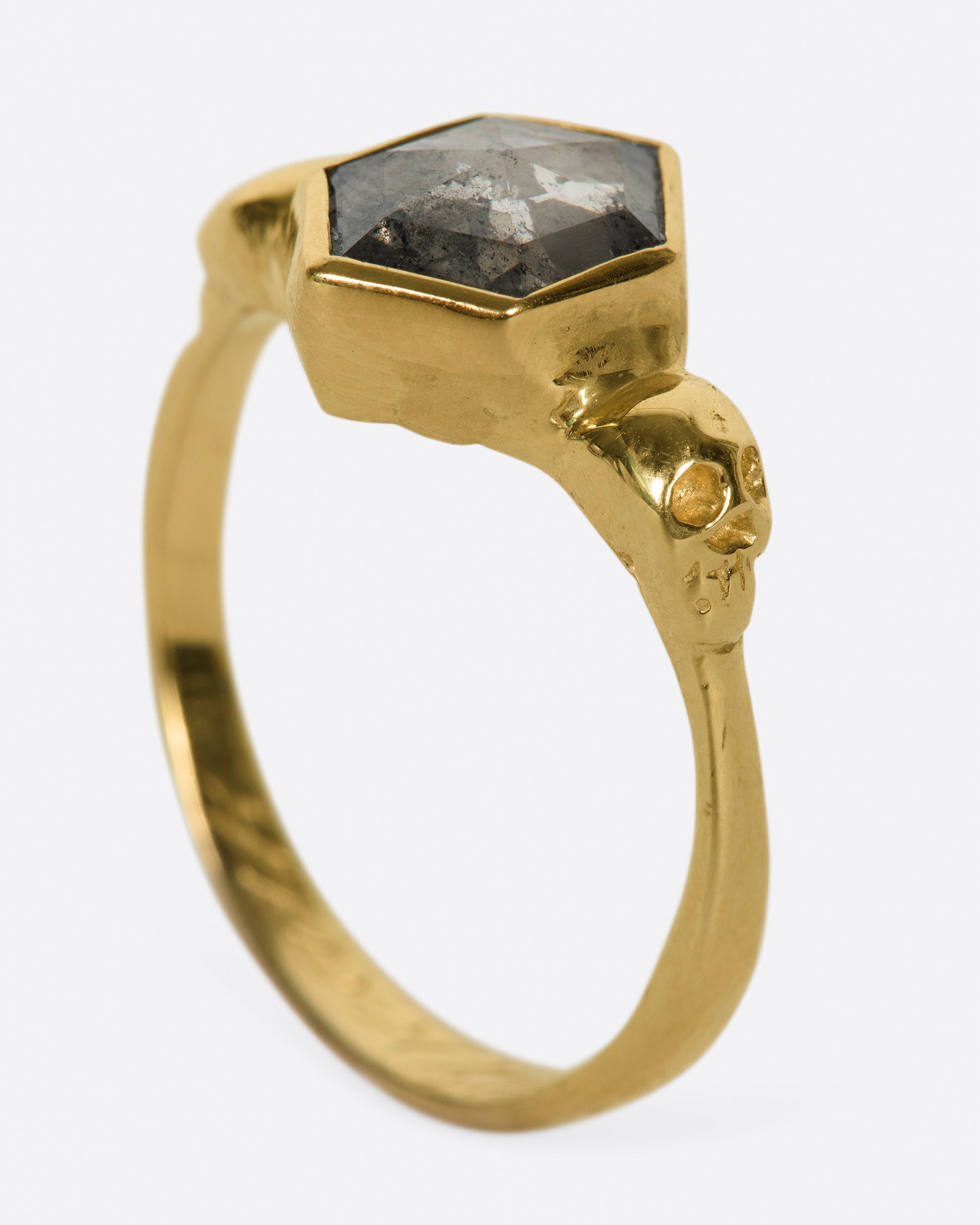 A bezel set, hexagonal, salt & pepper diamond ring with skulls on either side.