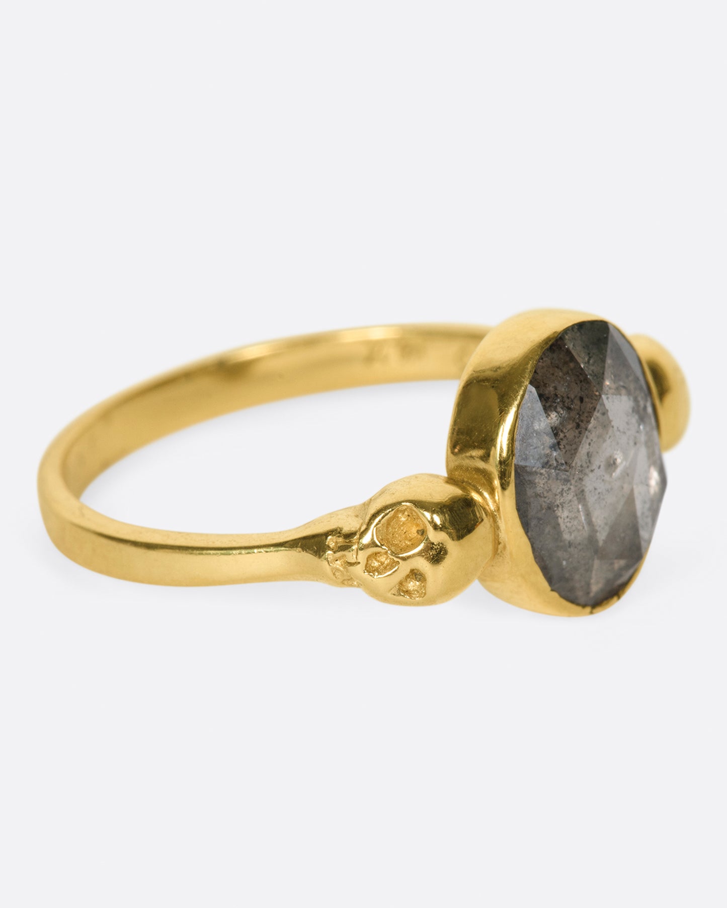 side view of a yellow gold margaret cross memento mori ring with a large oval salt and pepper diamond center set between two yellow gold skulls