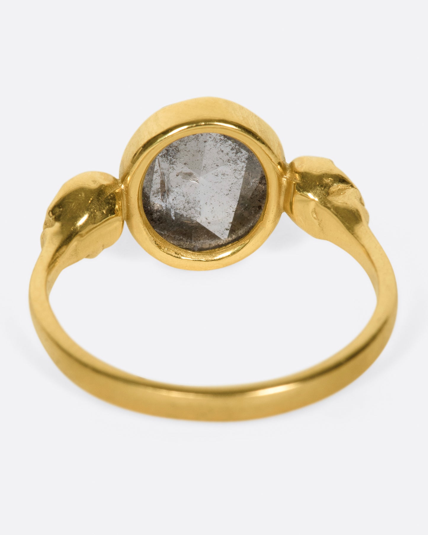 side view of a yellow gold margaret cross memento mori ring with a large oval salt and pepper diamond center set between two yellow gold skulls