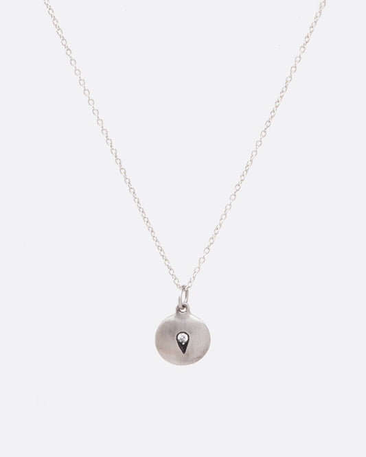 View of silver disc pendant with embedded teardrop design featuring small diamond hanging from silver chain