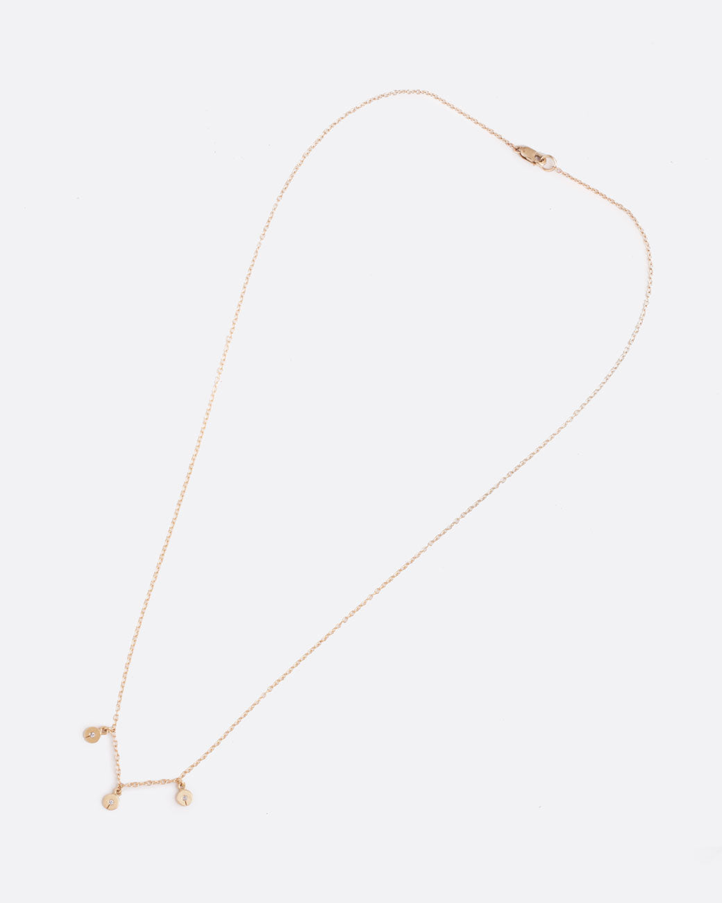 Far out birds eye view of necklace with three single grey diamonds with a slit in the bottom hanging from a yellow gold chain.