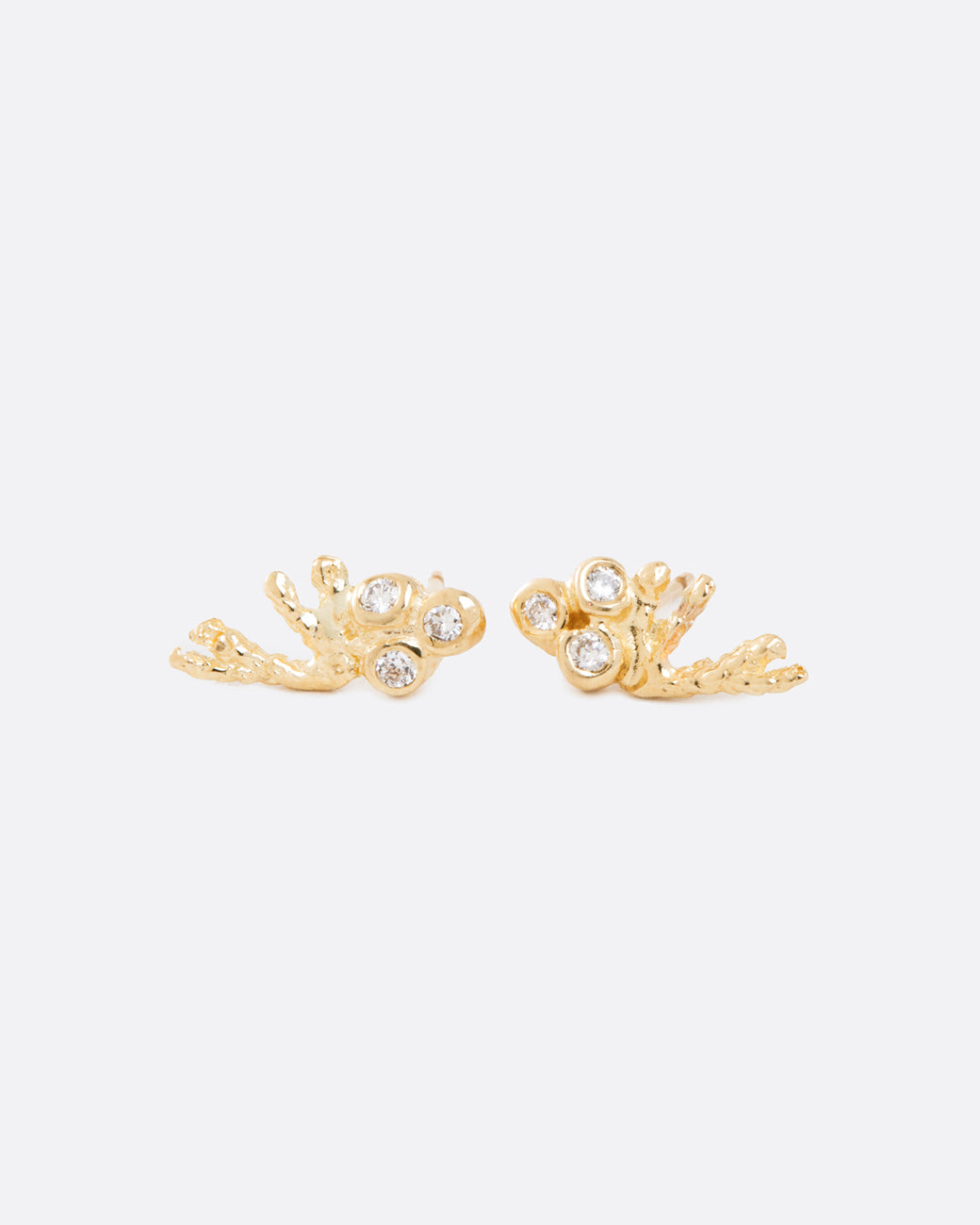 two yellow gold earrings with a trio of diamonds bezel set, and a yellow gold branch extending to the side.