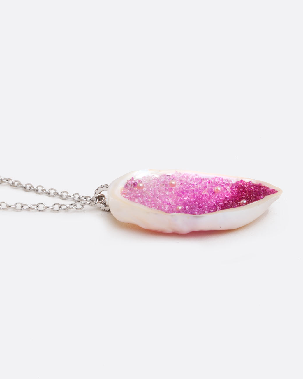 Close up side view of a large freshwater souffle pearl carved out and lined with ombre pink sapphires on a pendant with seed pearl accents and a pave diamonds.