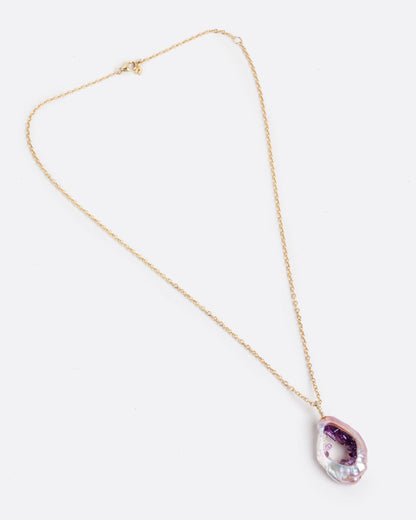 A large soufflé pearl open in the center and filled with pearls and amethysts, hanging from a cable chain and diamond bail. Shown lying flat from the front with clasp closed.