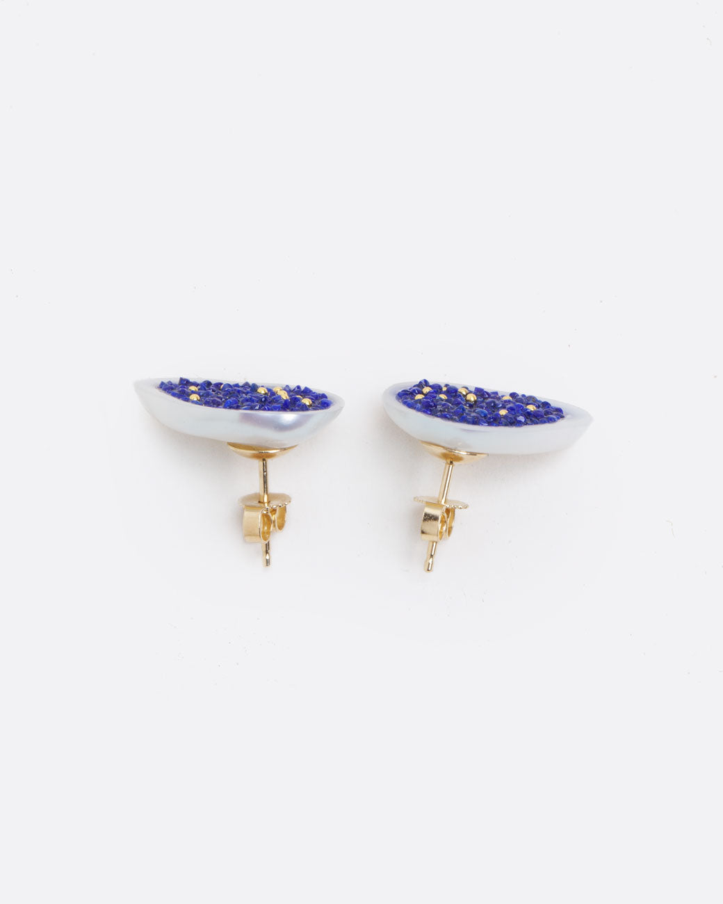 two earrings of a white souffle pearl that has been hollowed out and filled with small lapis pieces and small gold beads. with a yellow gold post back and yellow gold butterfly backing. view from above to show the backing and how flat the pearl is.