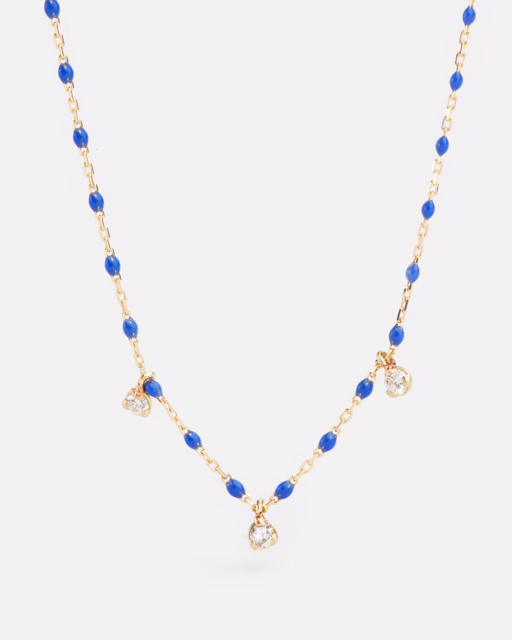 Close up birds eye view of yellow gold chain necklace with small blue resin beads with three diamond pendants alternating every two beads from the bottom of the necklace.