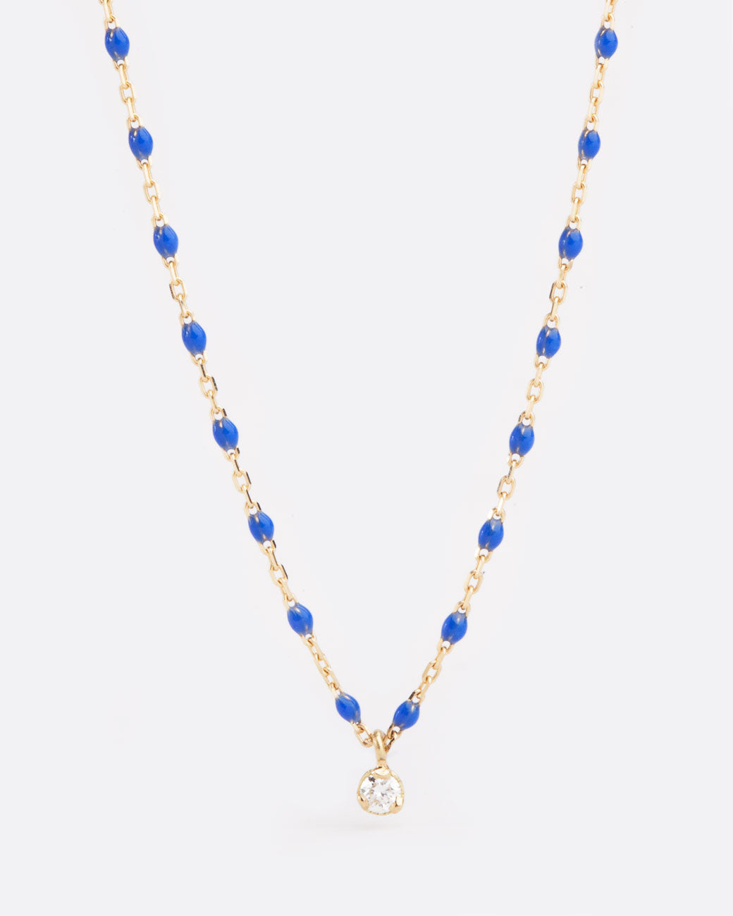 Close up birds eye view of yellow gold chain necklace with small blue resin beads with single diamond pendant