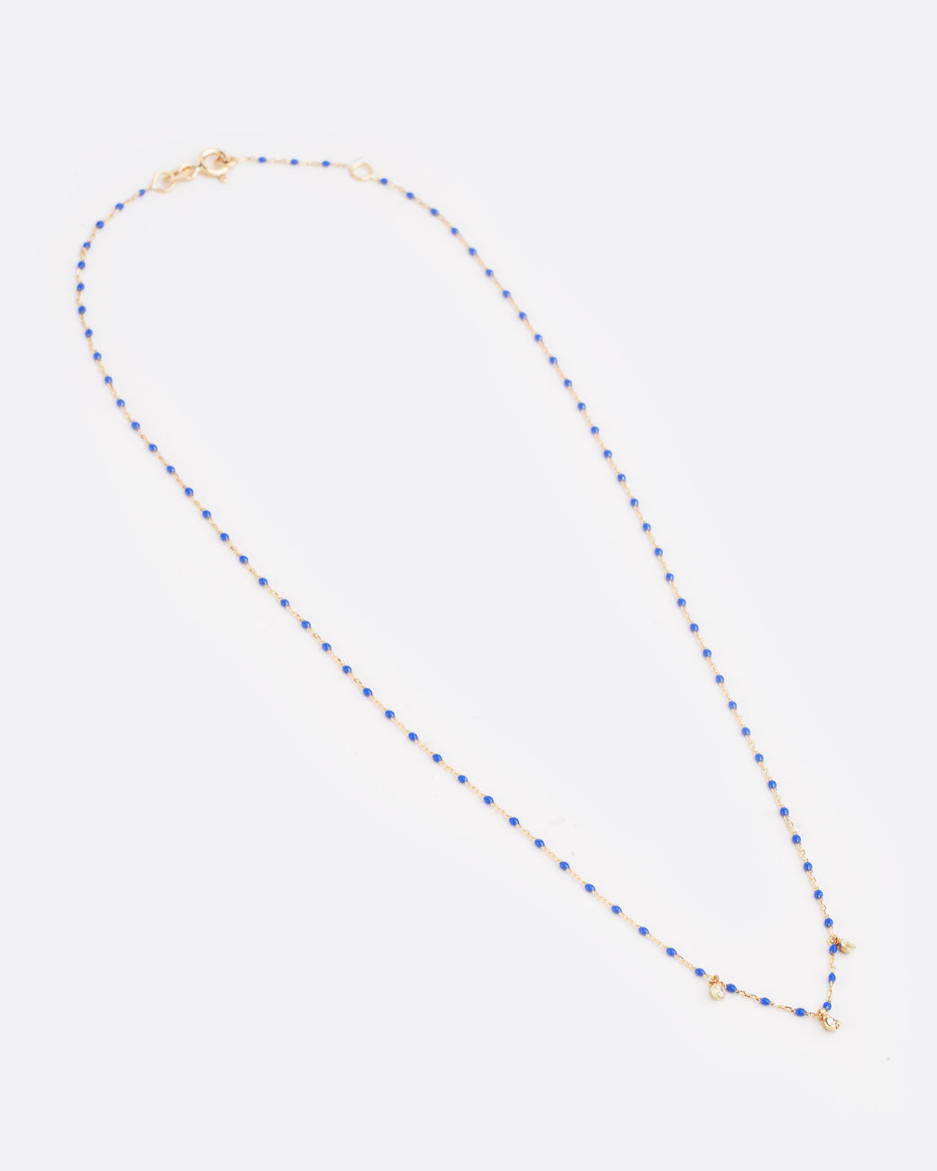 Far out birds eye view of yellow gold chain necklace with small blue resin beads with three diamond pendants alternating every two beads from the bottom of the necklace with clasp closed.