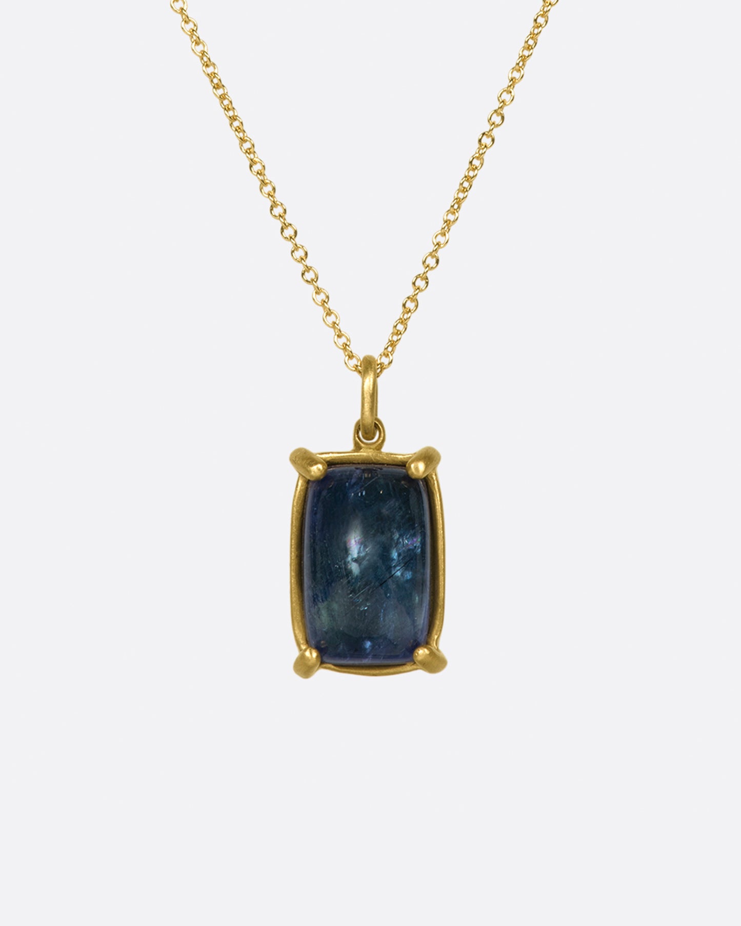 A large, rectangular tanzanite cabochon pendant set in matte gold prongs on a cable chain necklace.