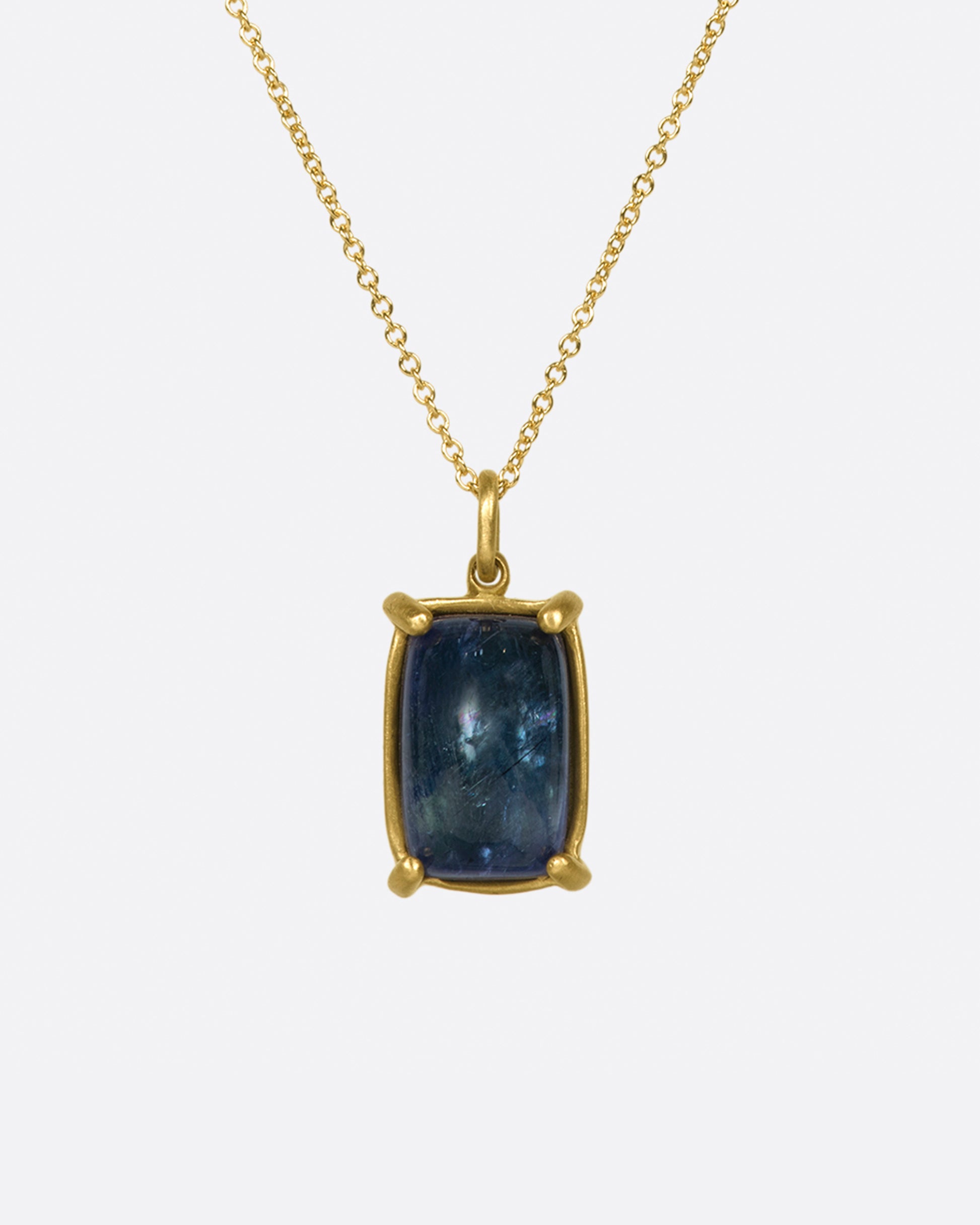 A large, rectangular tanzanite cabochon pendant set in matte gold prongs on a cable chain necklace.