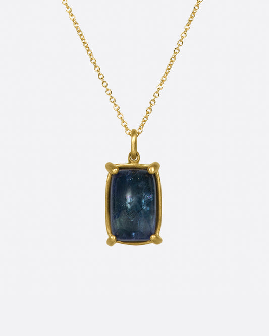 A large, rectangular tanzanite cabochon pendant set in matte gold prongs on a cable chain necklace.
