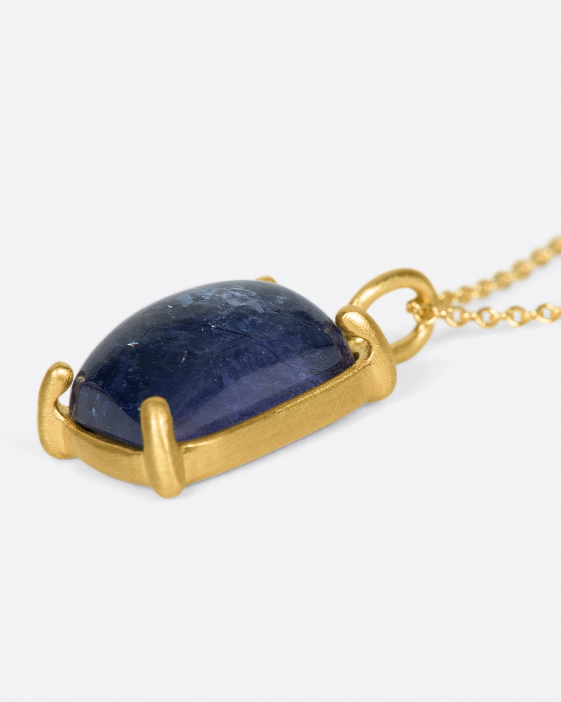 A large, rectangular tanzanite cabochon pendant set in matte gold prongs on a cable chain necklace.