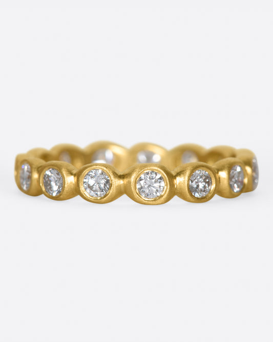 An eternity band of bezel set white diamonds in matte gold settings.