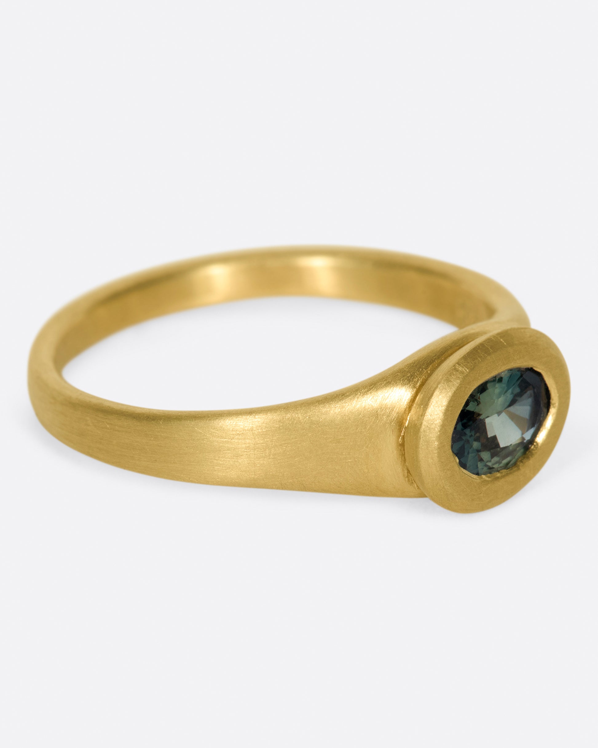 A one of a kind satin-finish gold ring with an oval blue-green Parti sapphire at its center.