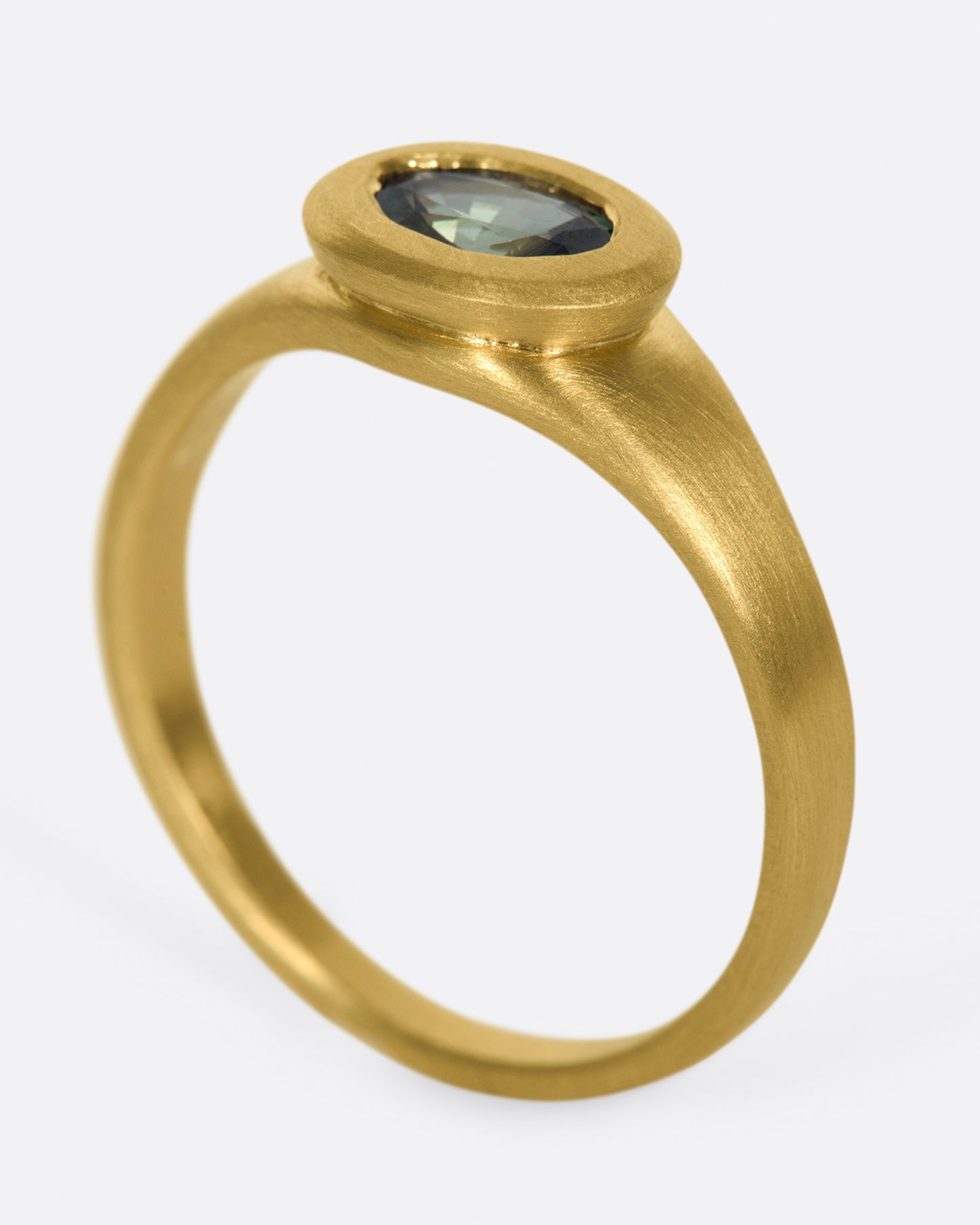 A one of a kind satin-finish gold ring with an oval blue-green Parti sapphire at its center.