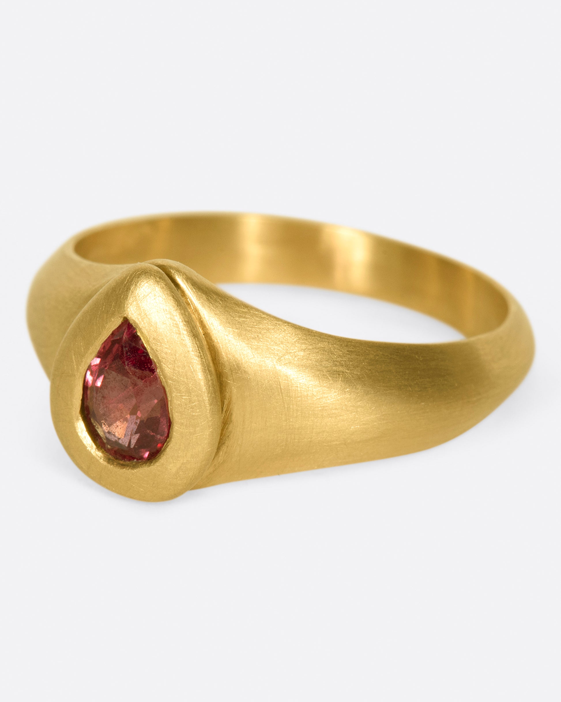 A one of a kind gold ring with a teardrop shaped orangey-pink spinel at its center.