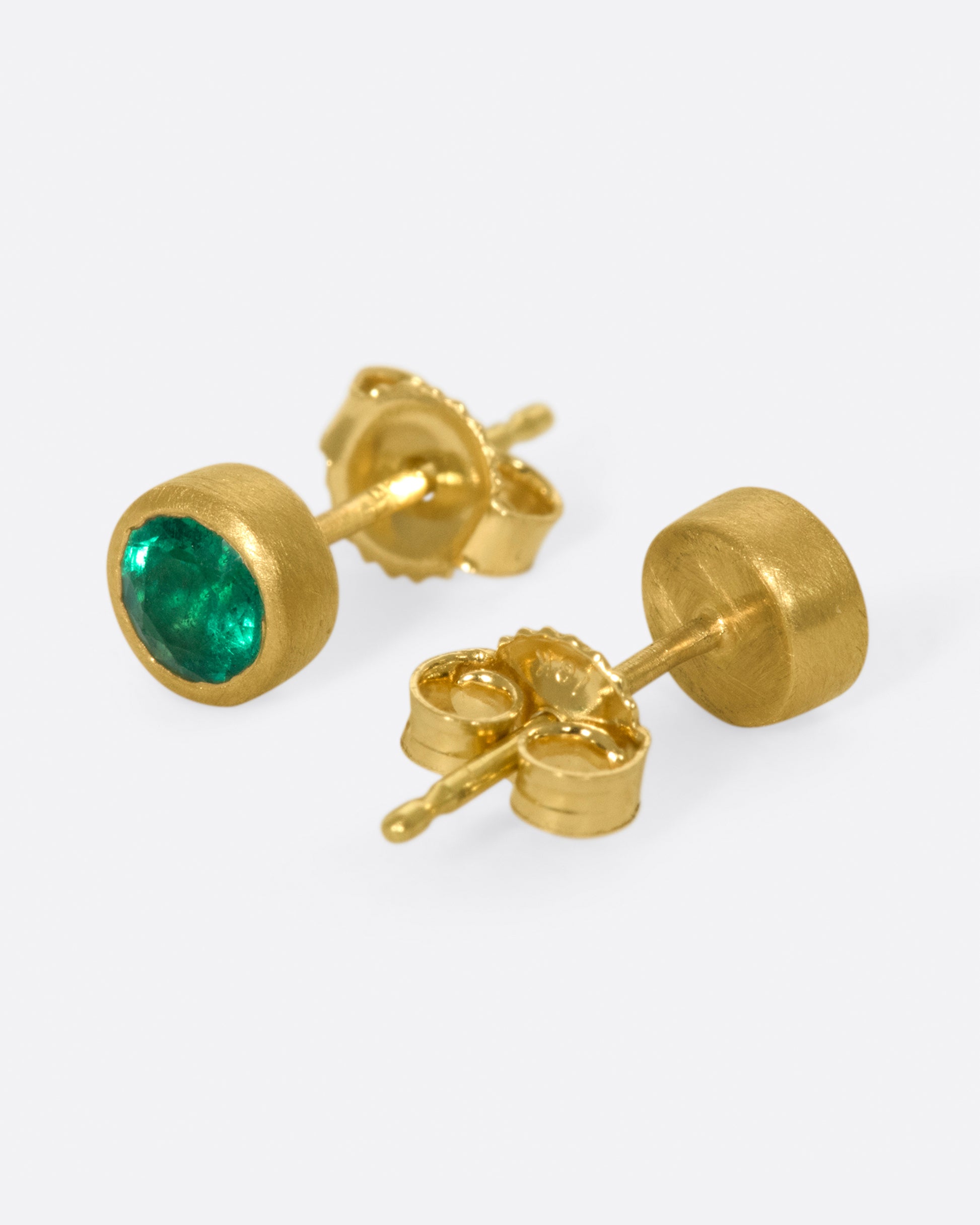 A pair of classic, solitaire earrings with vibrant emeralds set in matte gold bezels.