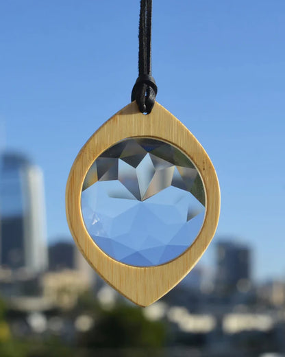 A bamboo monocle on a suede cord. Shown hanging in a window from the front.