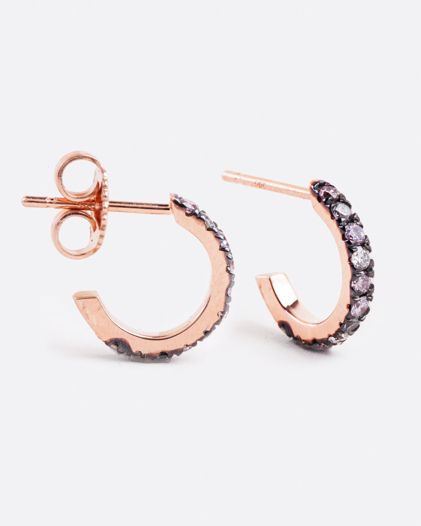 huggie hoop earrings with a stud post backing, they are rose gold with blackened settings around the grey, pink and white diamonds that are set along the huggie