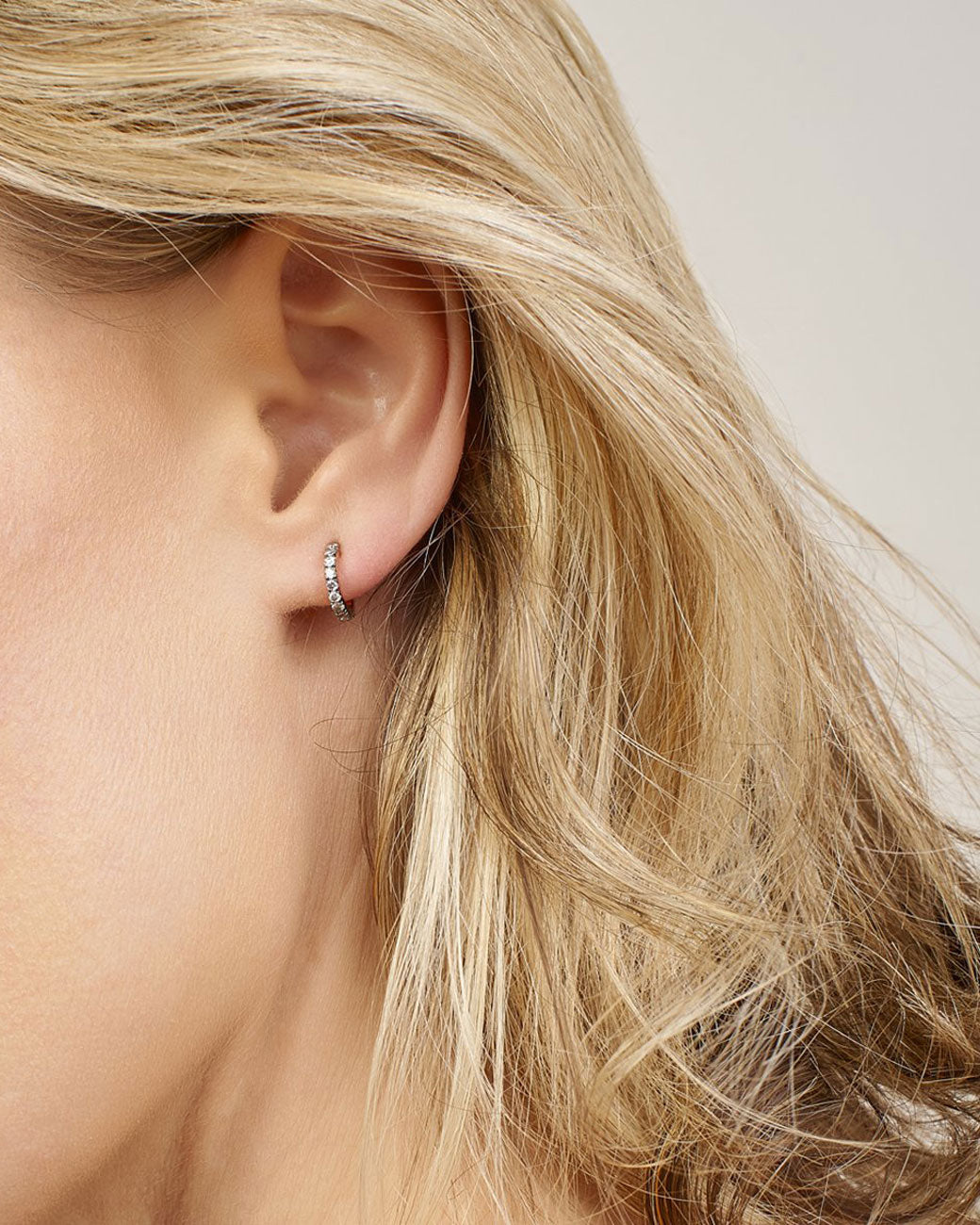 a womans ear with a little hoop on it. the hoop is hugging the ear lobe - there is no space between the two. the earring is pave.