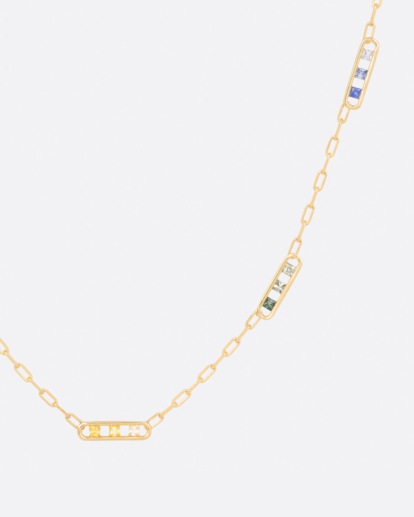 A yellow gold chain necklace with five stations containing princess cut rainbow sapphires, shown hanging on the right.