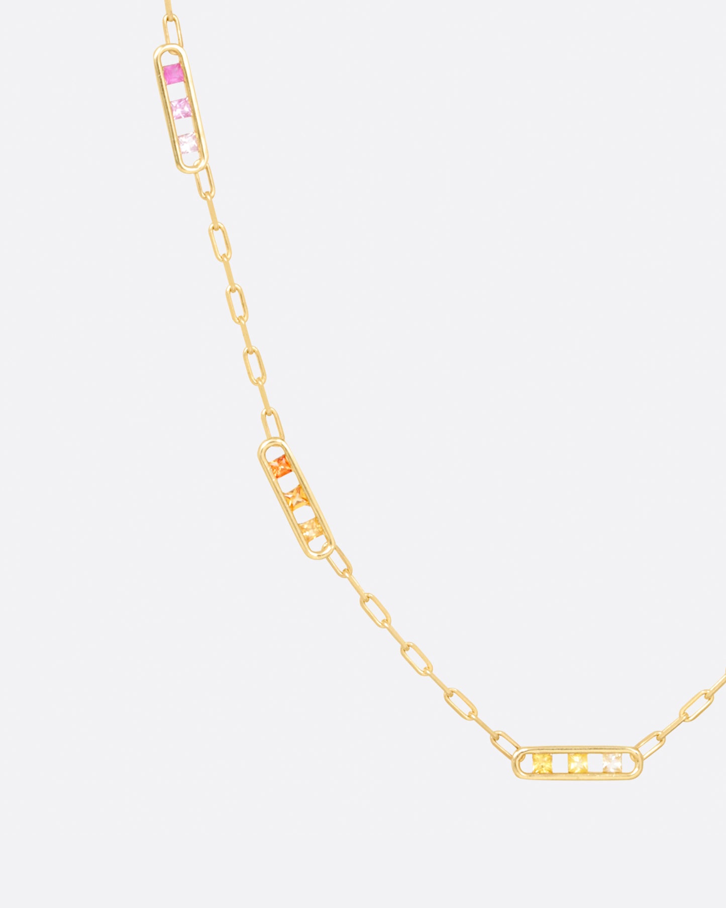 A yellow gold chain necklace with five stations containing princess cut rainbow sapphires, shown hanging on the left.
