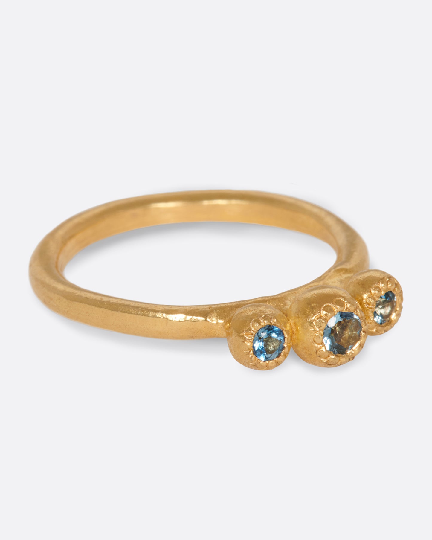 A handmade, high karat gold ring with three vibrant, bezel set aquamarines.