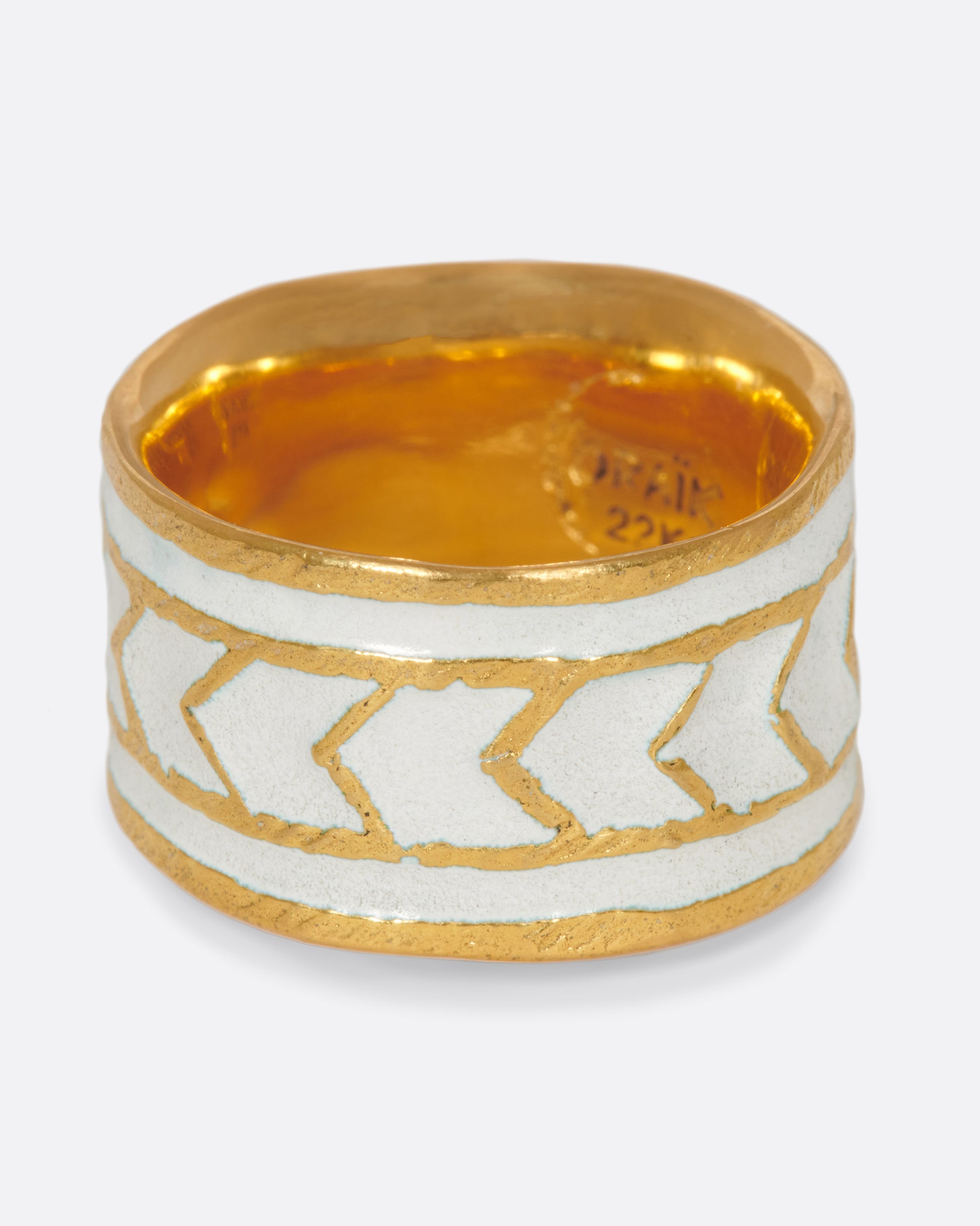 A handcrafted gold band with a path of consecutive arrows in white enamel.