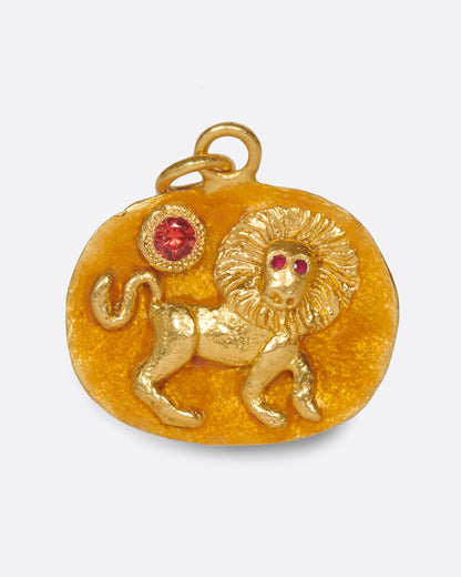 A yellow gold medallion with a hand-sculpted Leo icon with ruby eyes and an orange sapphire sun. Shown from the front.