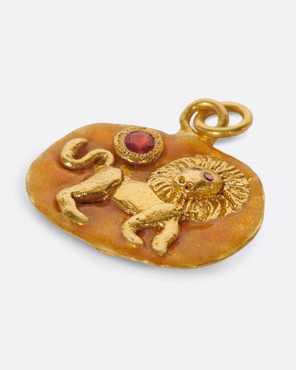 A yellow gold medallion with a hand-sculpted Leo icon with ruby eyes and an orange sapphire sun. Shown lying flat.