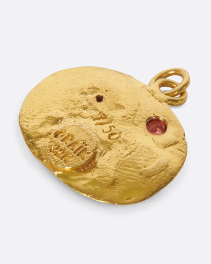 A yellow gold medallion with a hand-sculpted Leo icon with ruby eyes and an orange sapphire sun. Shown from the back.